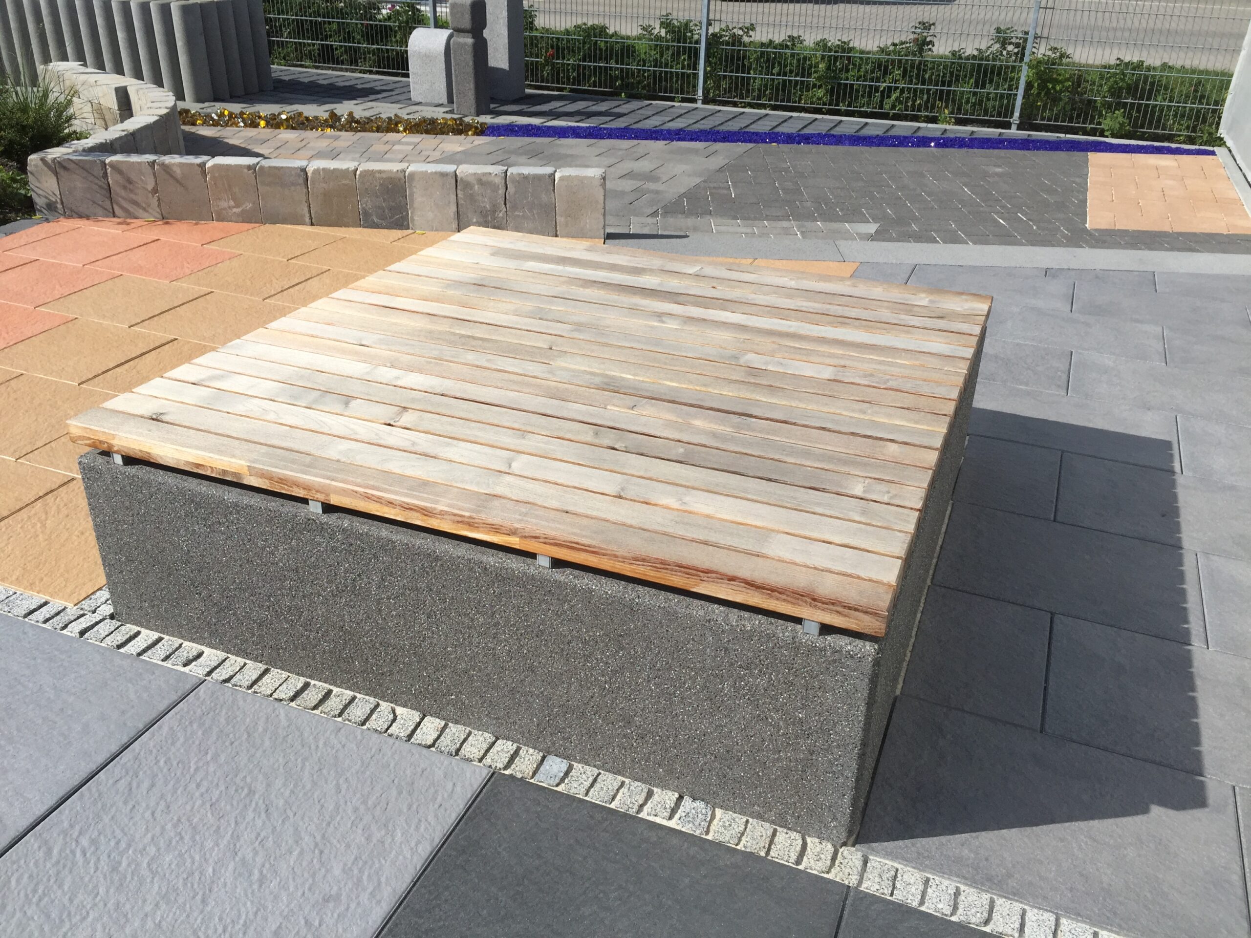Sitzbank mit Holzauflage auf gepflastertem Platz