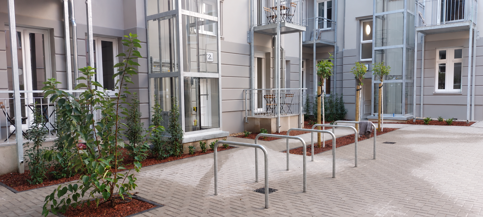 Neu angelegter Innenhof mit Pflasterflächen, jungen Bäumen, Pflanzbeeten und Fahrradstellplätzen